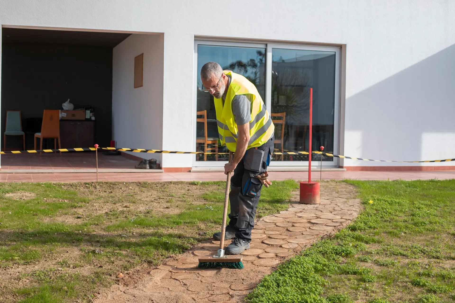 Construction worker cleaning pathway in safety vest.