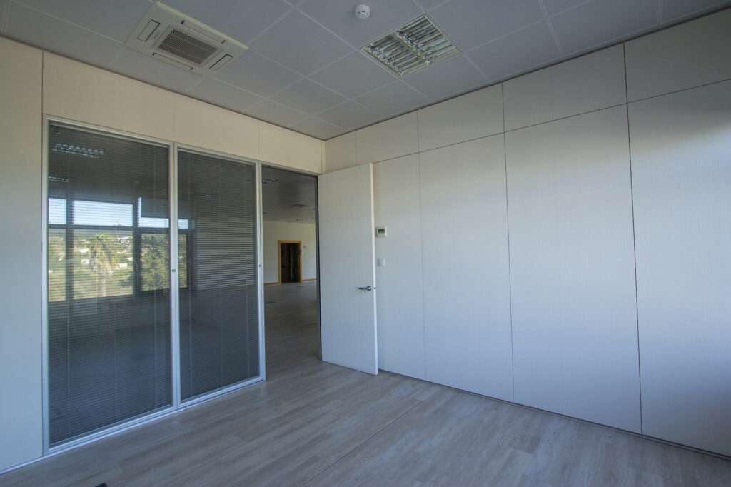 Modern empty office room with glass partition, white panel walls, and wooden flooring.