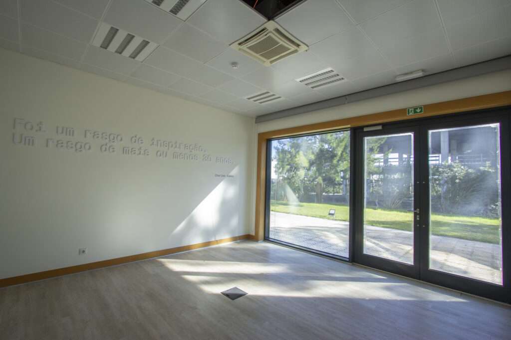 Empty office room with large glass doors, wooden flooring, and natural outdoor view.